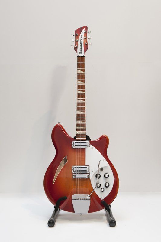A red electric guitar is sitting on a stand on a white surface.