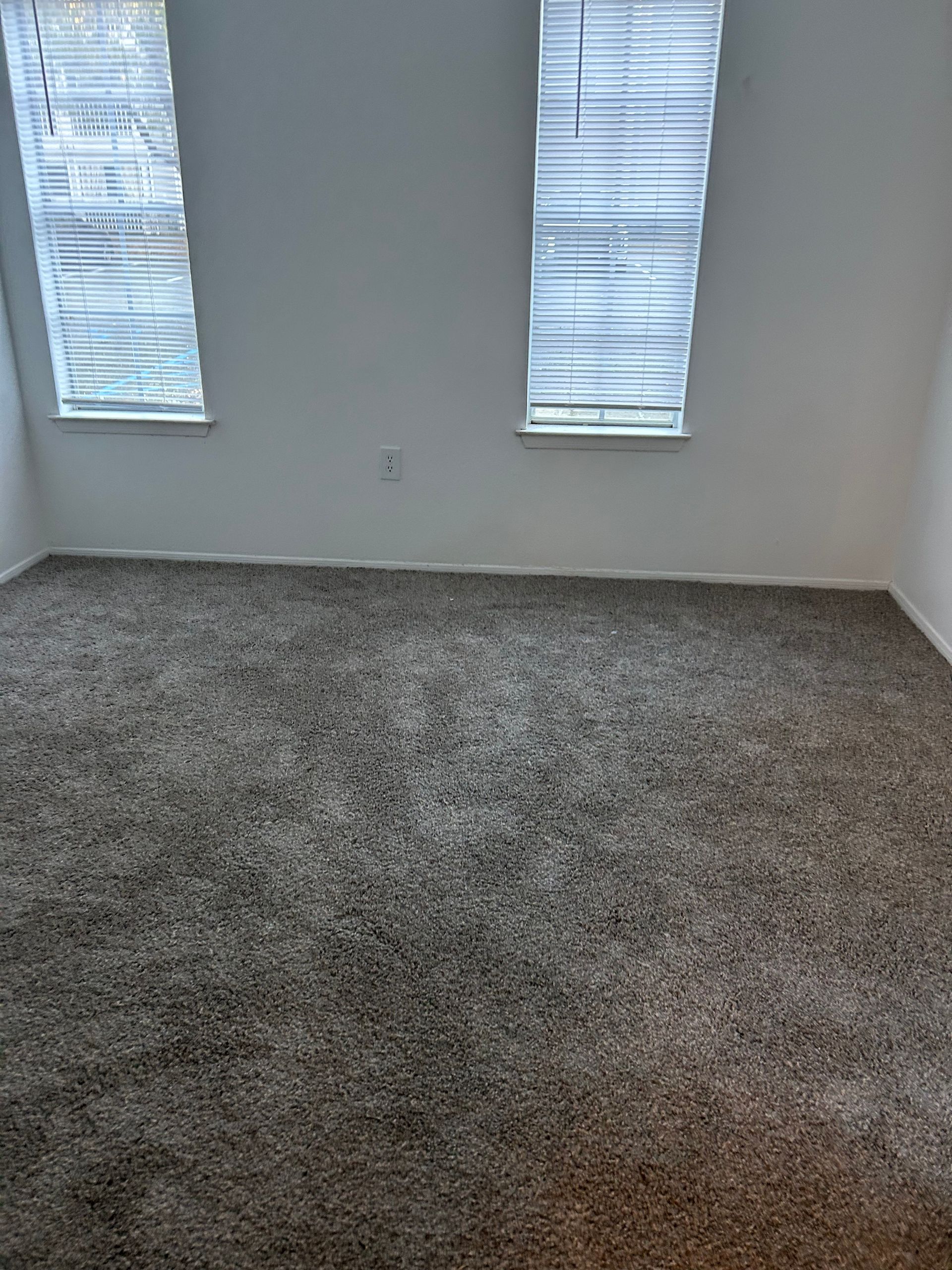 Empty room with gray carpet and two windows with blinds. White walls.