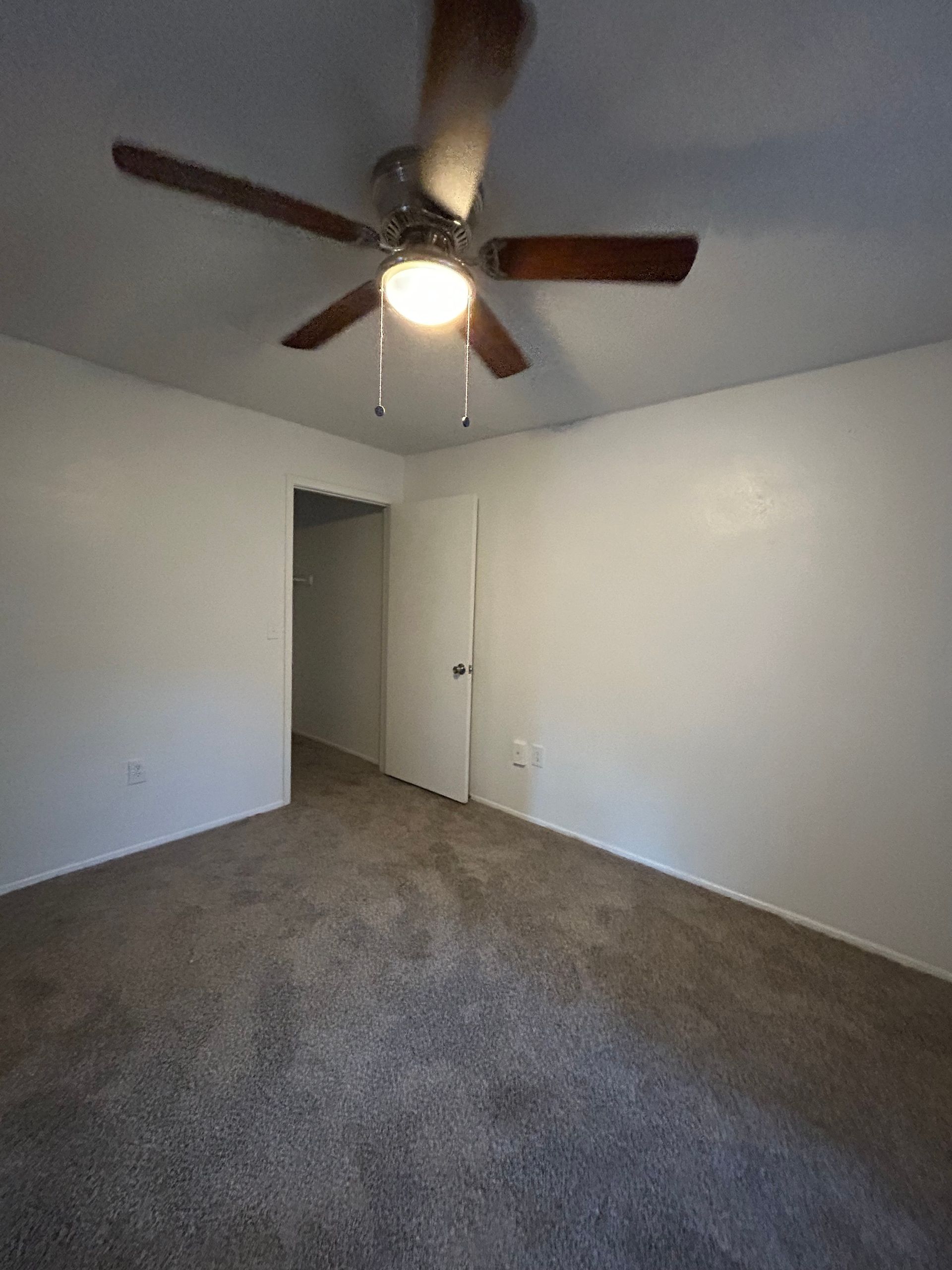 Empty room with white walls, brown carpet, ceiling fan, and a doorway.