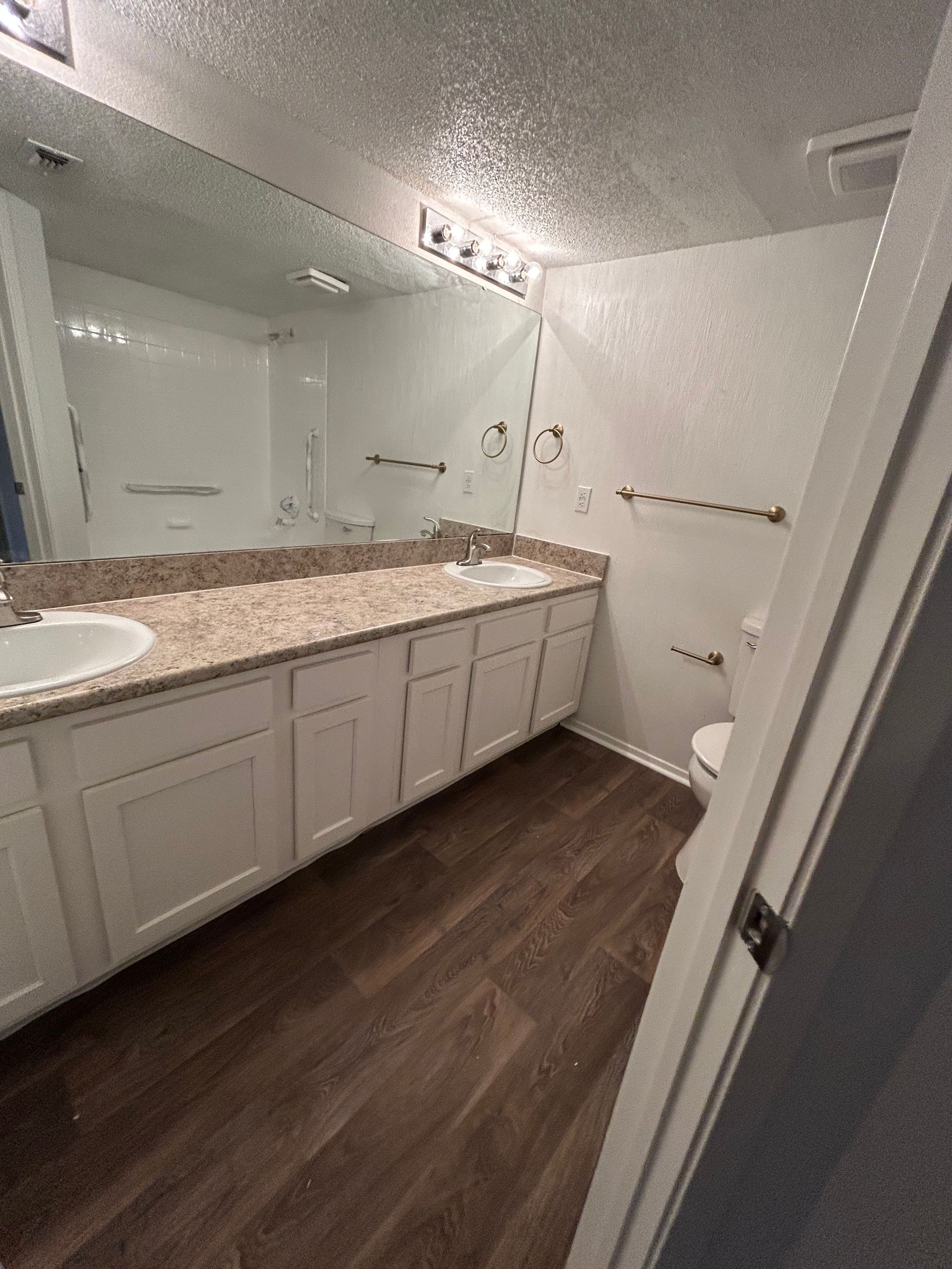 Bathroom with white cabinets, wood-look floor, large mirror, and toilet.
