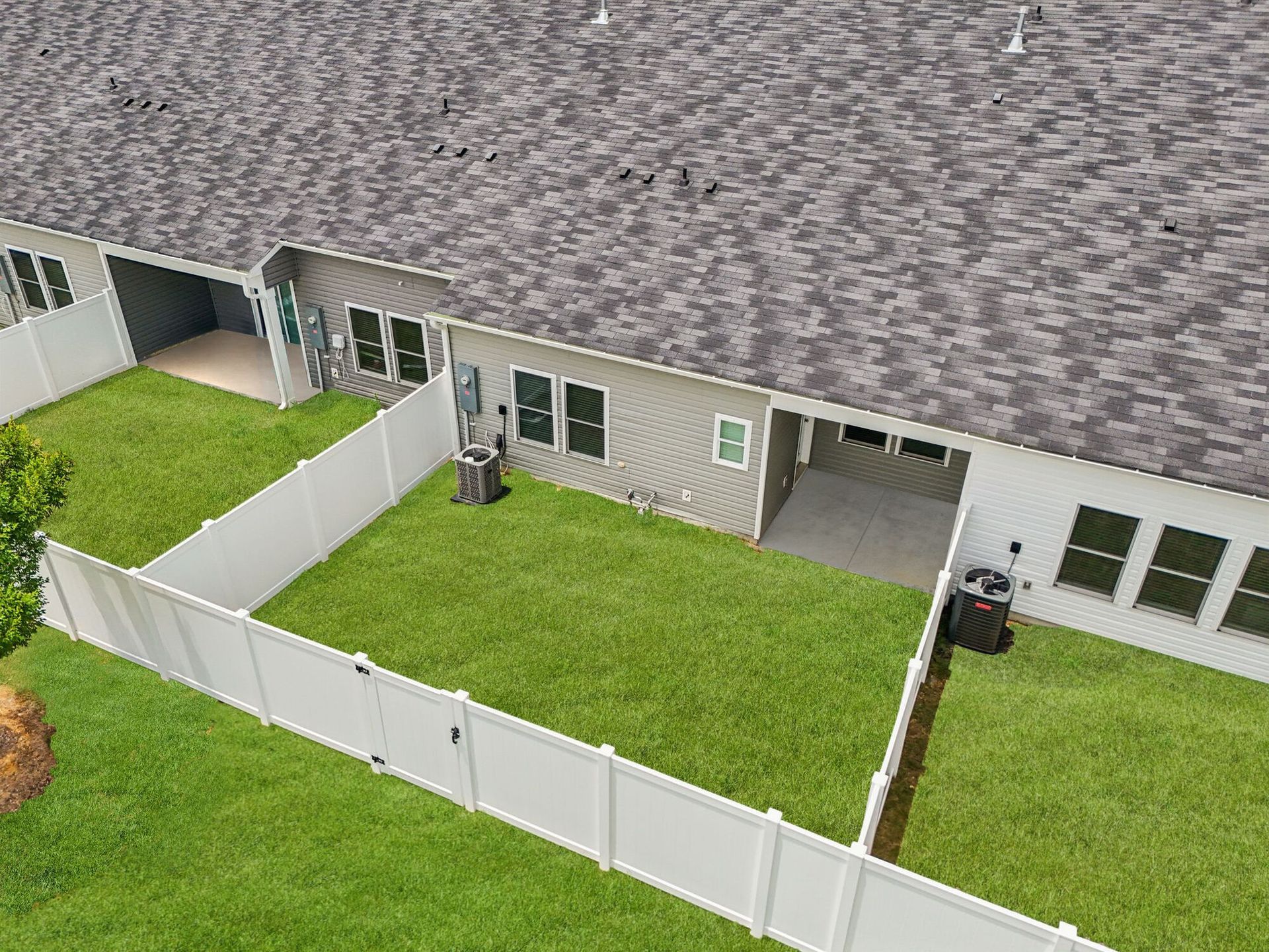 Overhead view of connected townhomes with fenced backyards, green grass, and gray roofs.