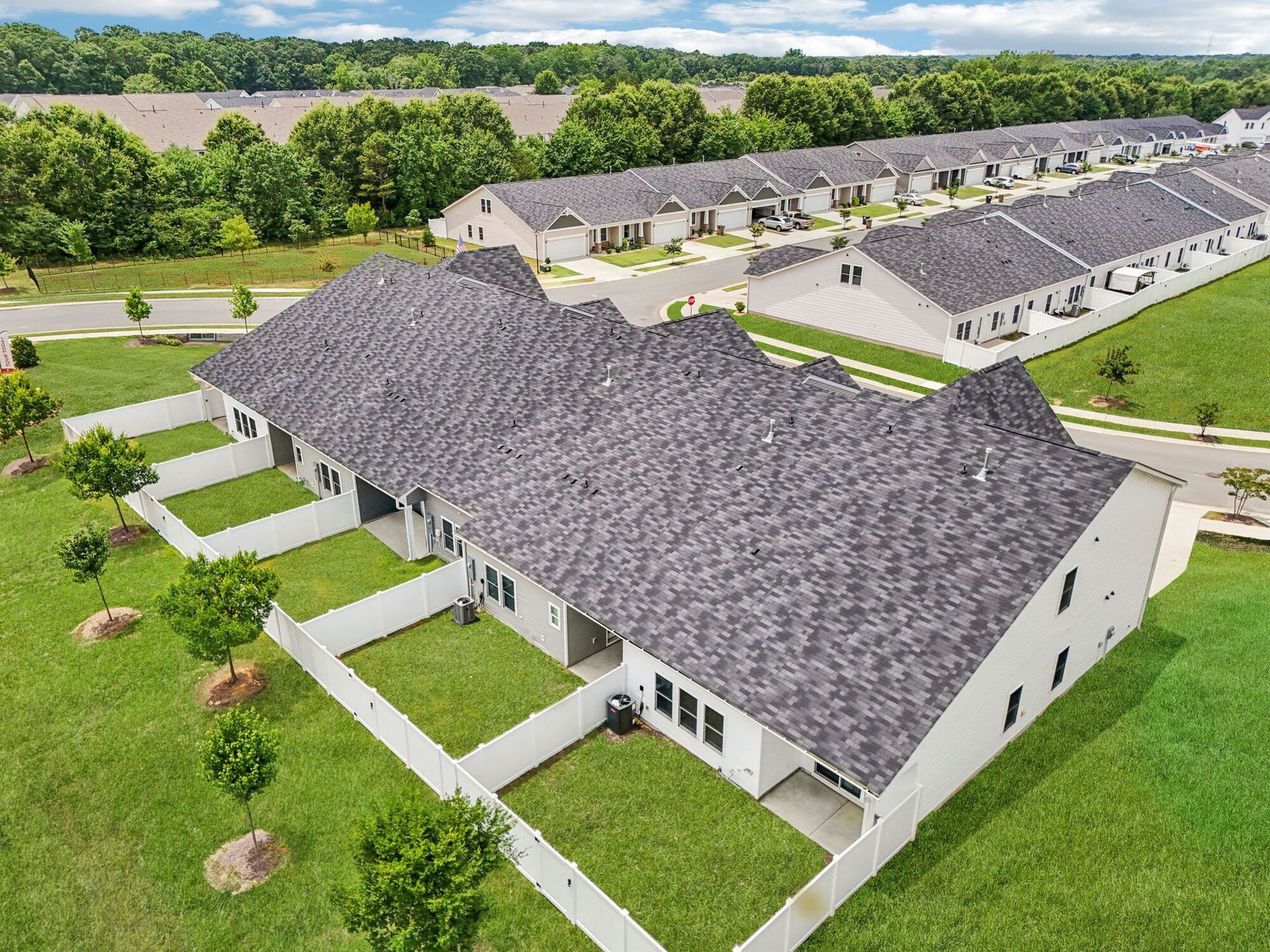 Aerial view of townhouses with gray roofs and white fencing in a grassy area.