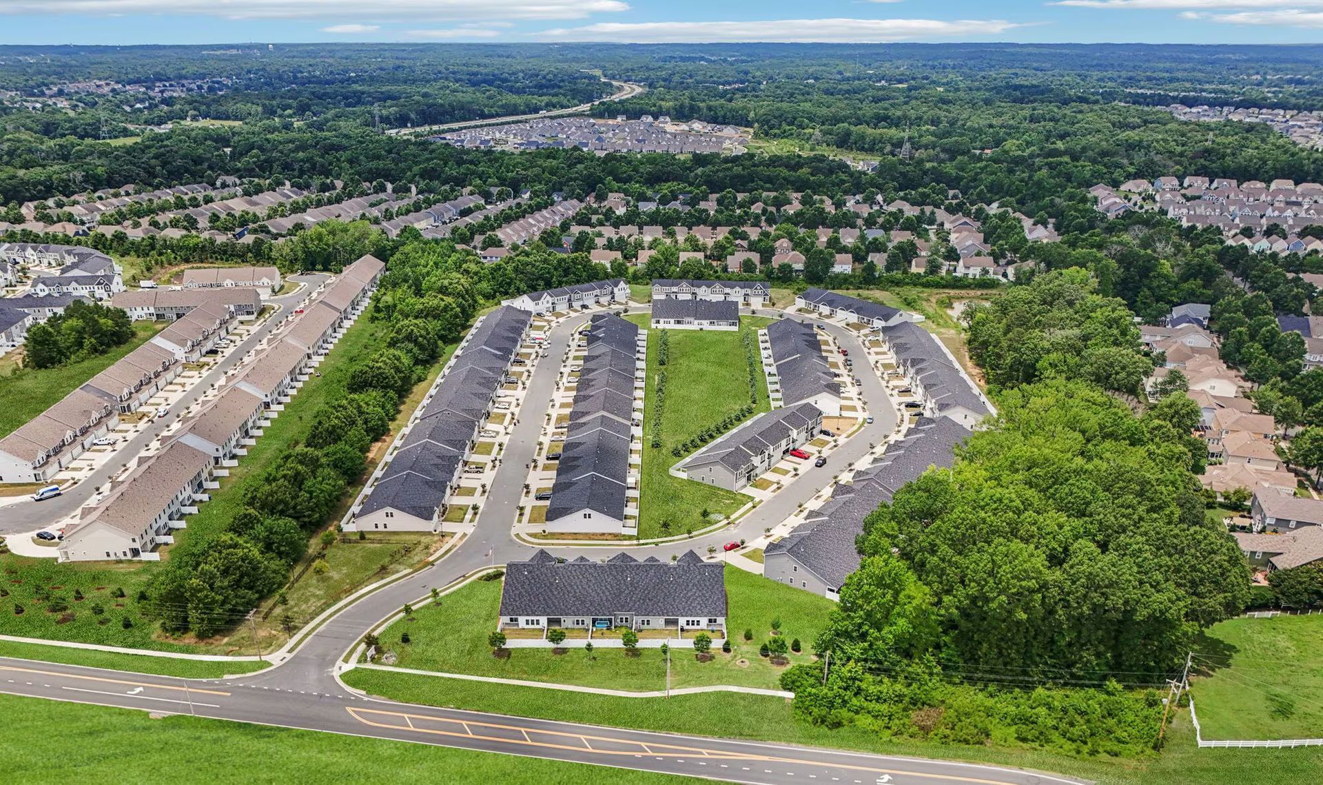 Aerial view of a suburban neighborhood with rows of townhouses and green space; sunny day.