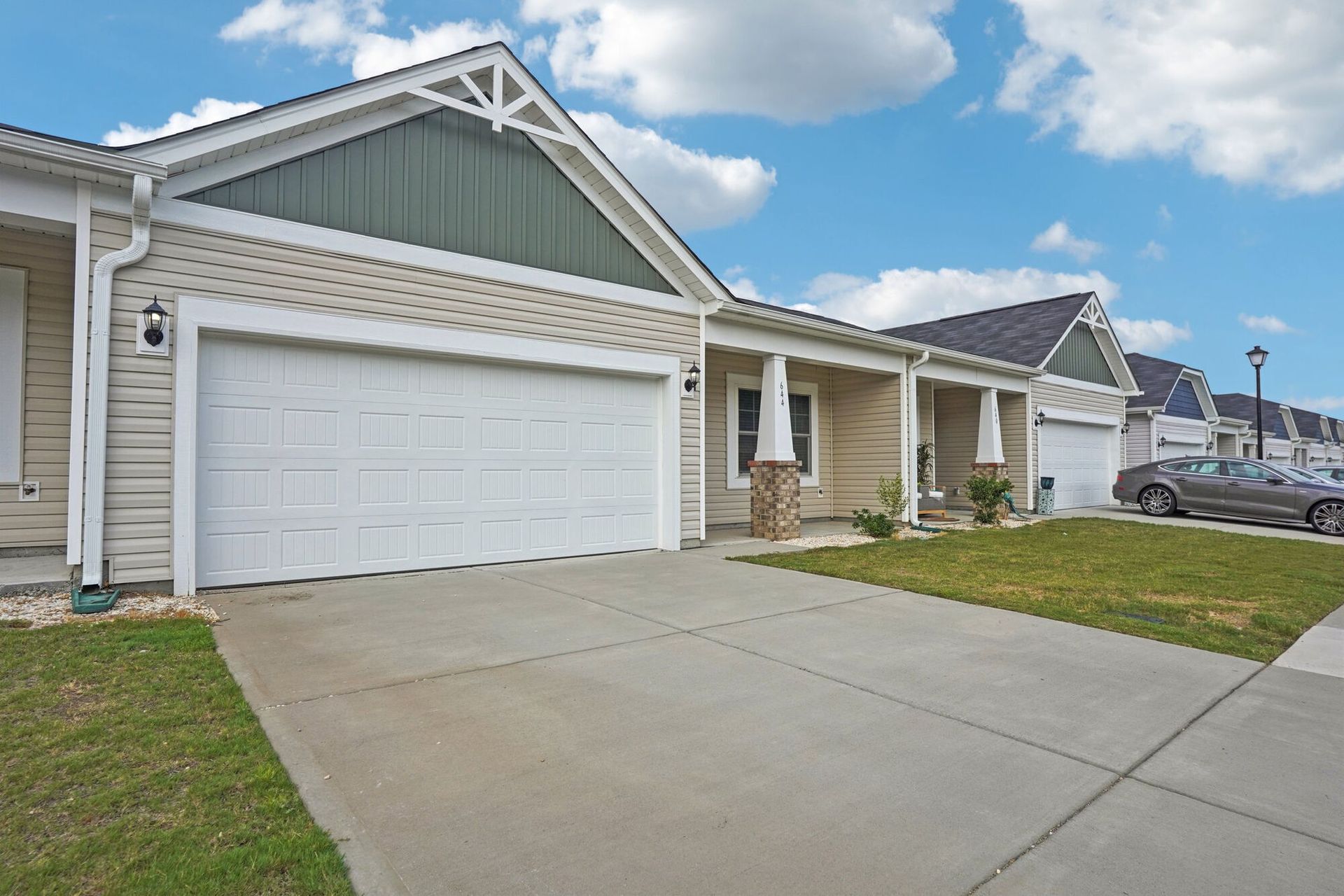 Row of beige townhomes with white garage doors and green gables; gray driveways, blue sky.