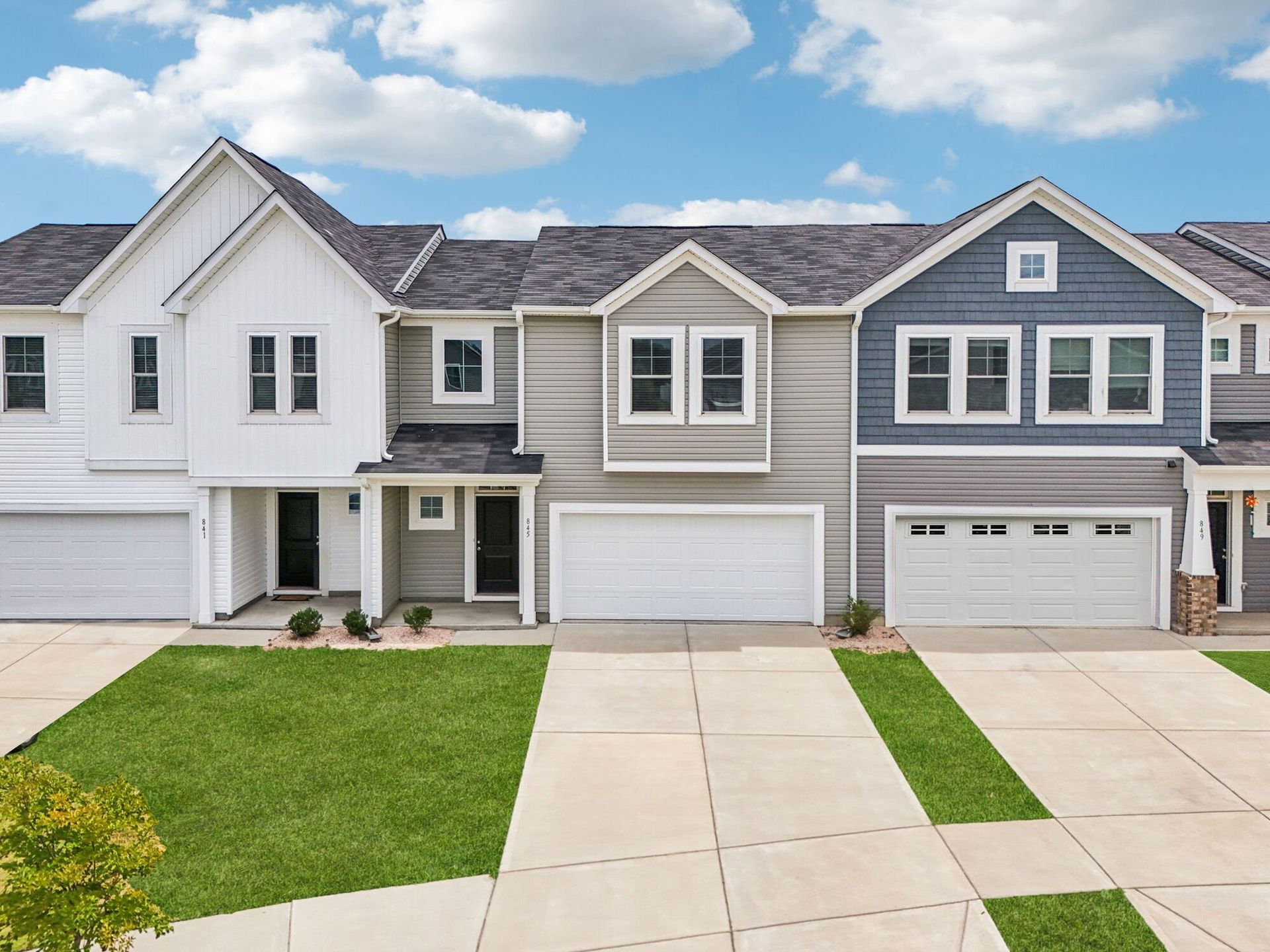Row of modern townhomes with light gray, white, and blue siding. Each has a garage and a small lawn.