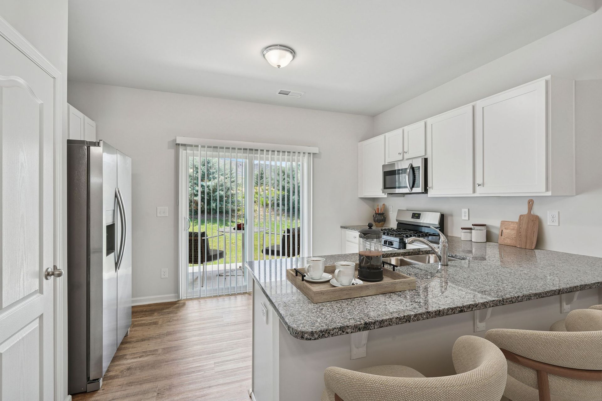 Modern kitchen with white cabinets, stainless steel appliances, and a granite island with seating; sliding glass door to backyard.