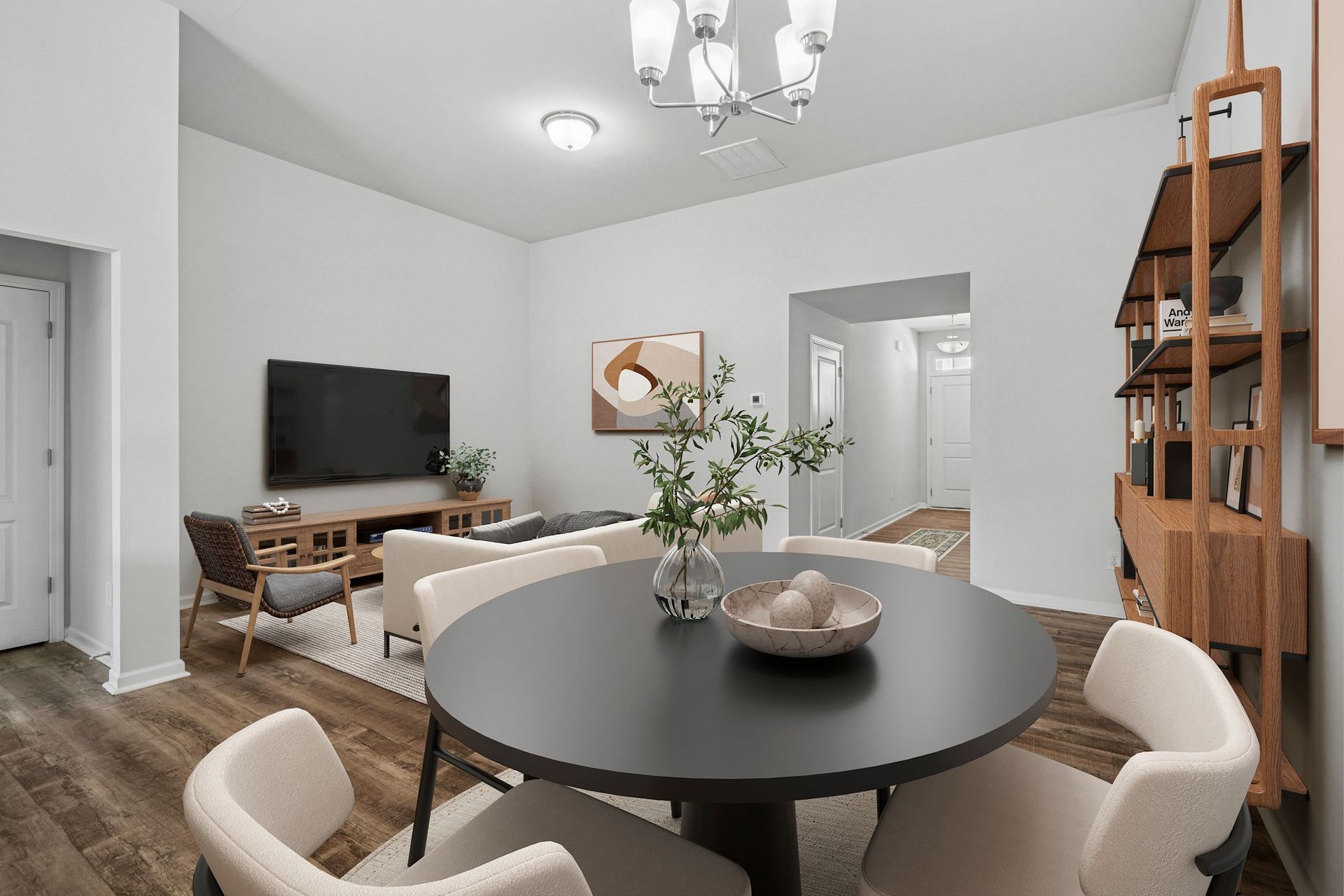 Dining area with a round black table and chairs, connected to a living area with a TV and shelving.