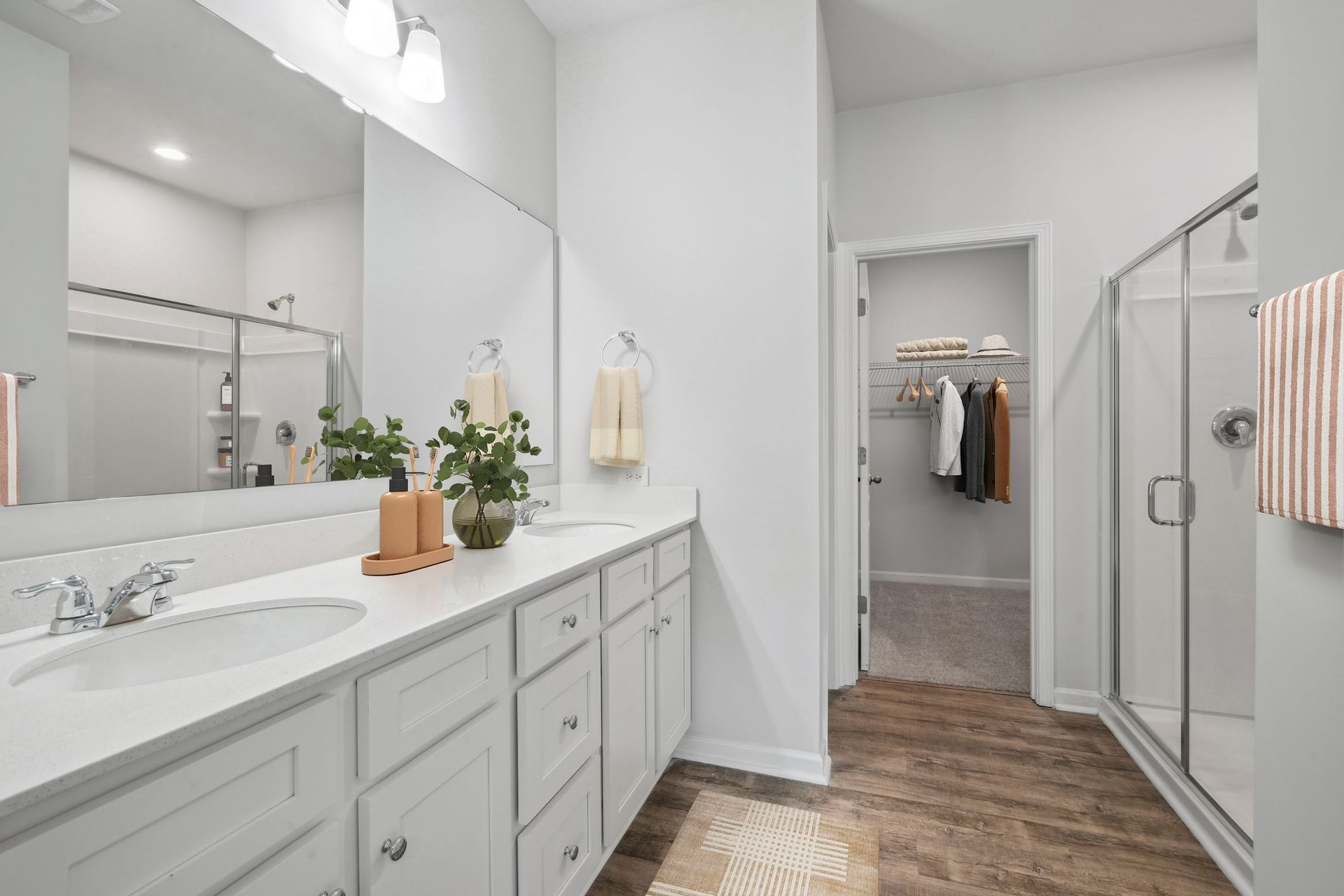 Bathroom with white cabinets, double sinks, large mirror, shower, and walk-in closet.