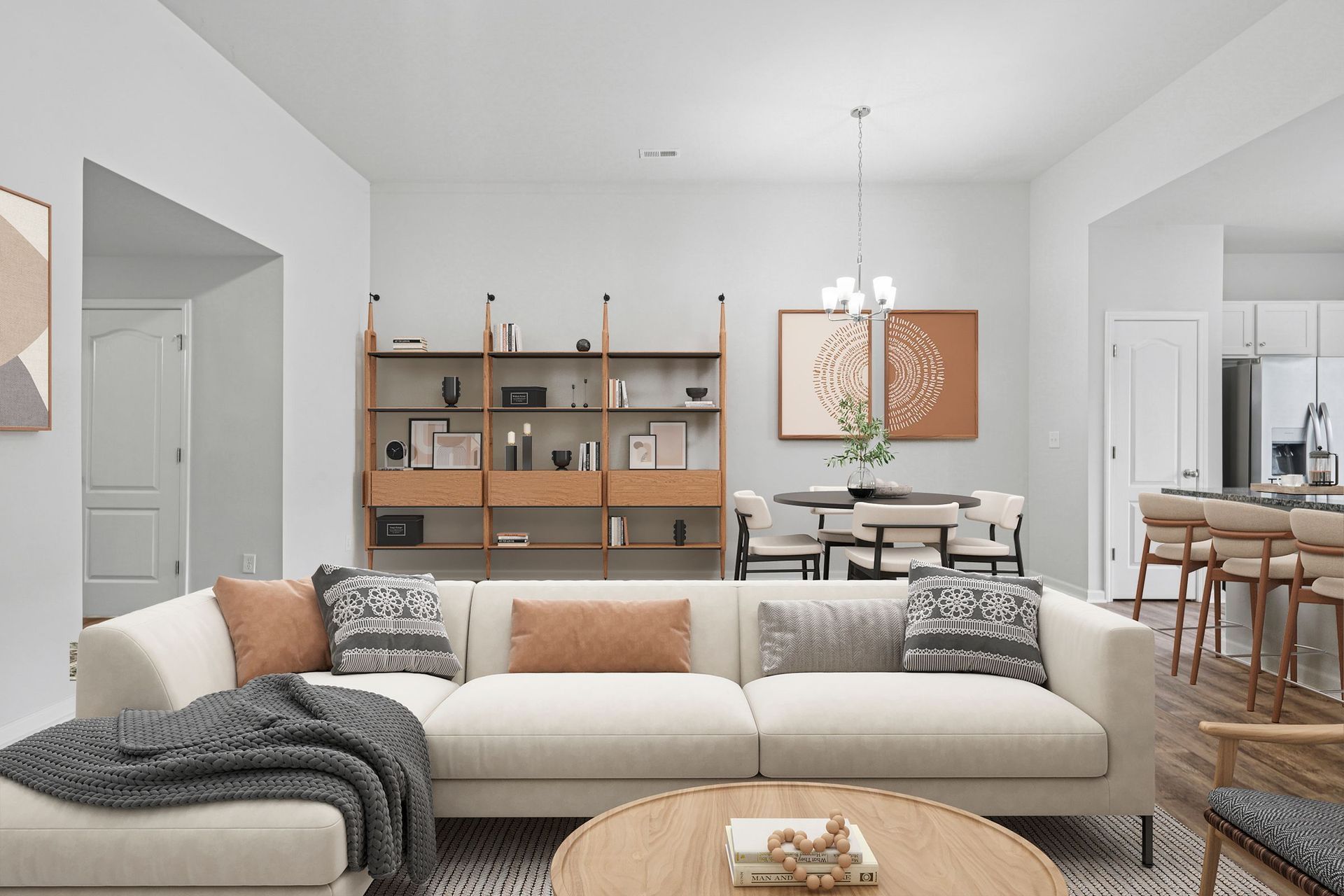 Living room with a sectional sofa, bookshelf, dining area, and kitchen. Neutral colors, natural wood accents.