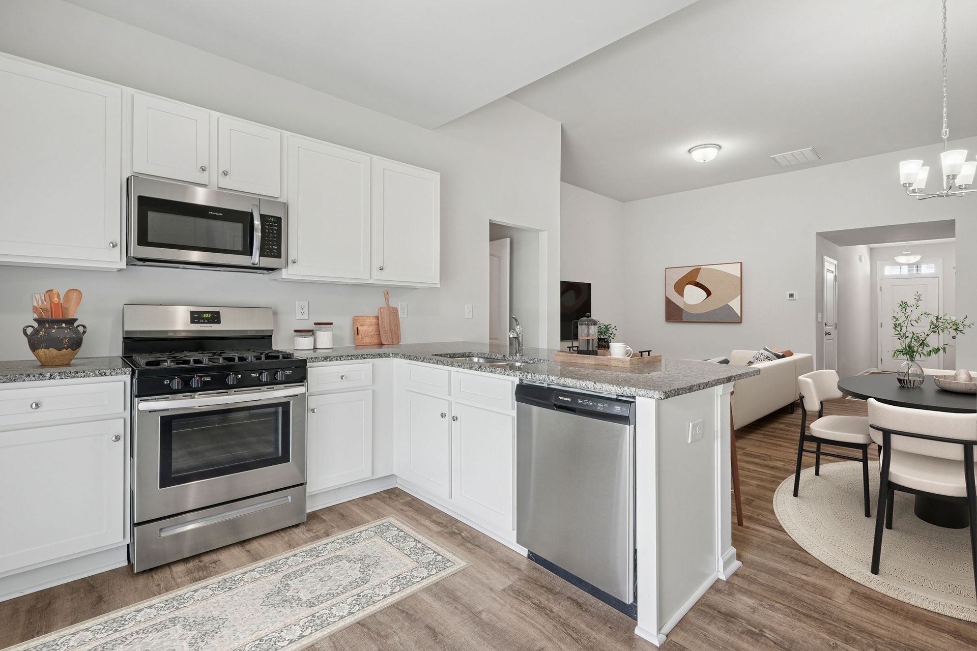 A modern kitchen with white cabinets, stainless steel appliances, and a granite countertop, open to a dining area.