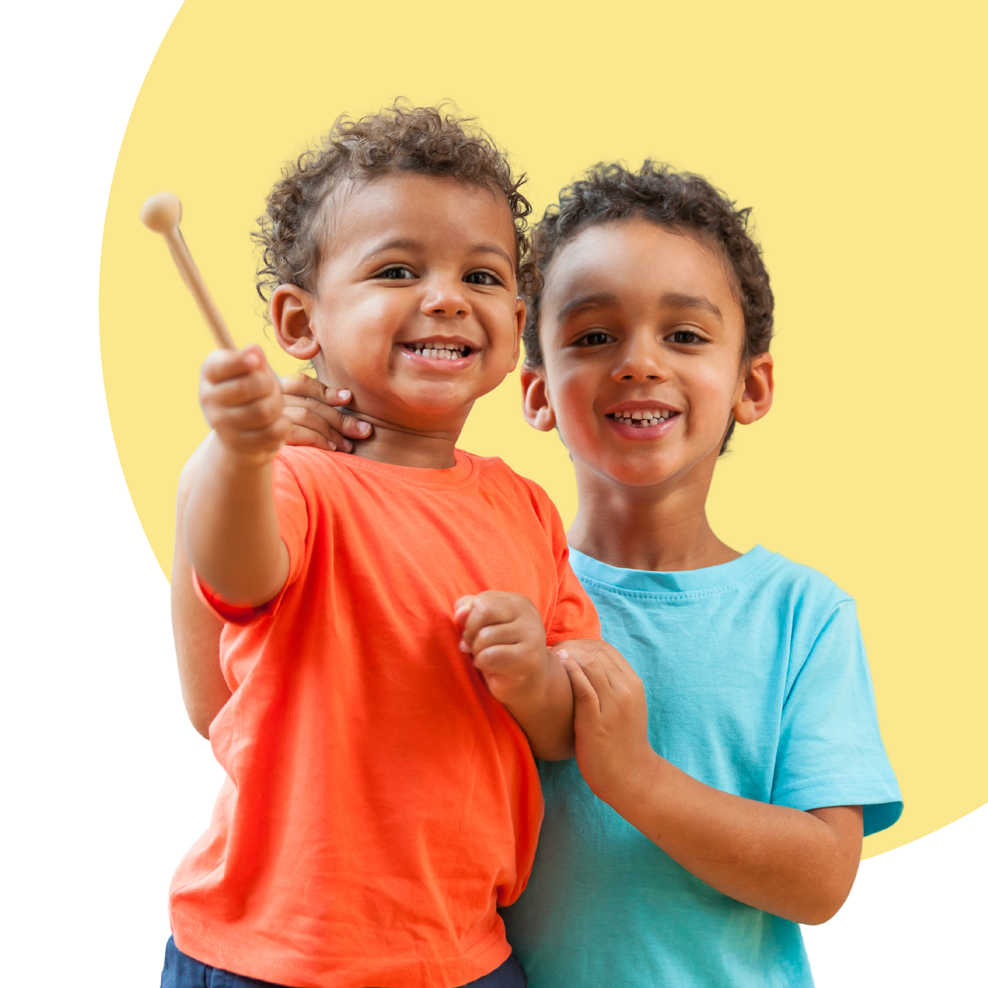 Two young children smiling, one holding a drumstick, against a yellow and white background.