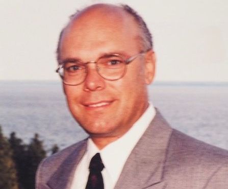 A man in a suit and tie stands in front of the ocean