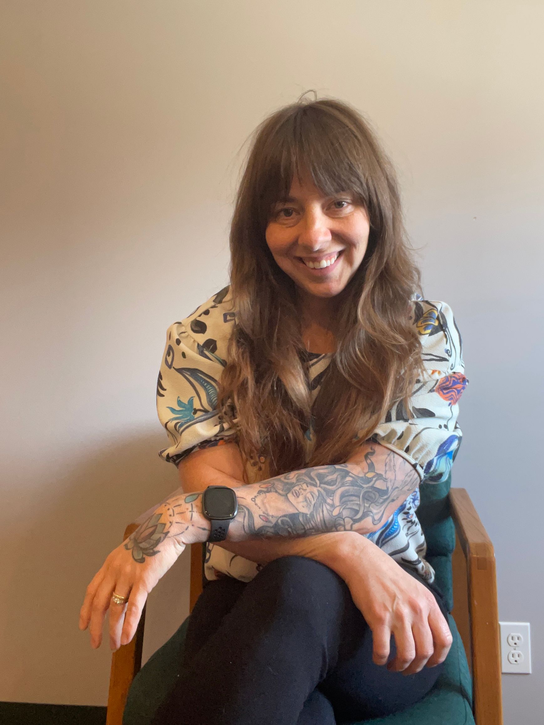 A woman with tattoos on her arms is sitting in a chair.