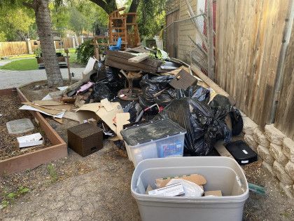 A pile of trash in a backyard next to a wooden fence.