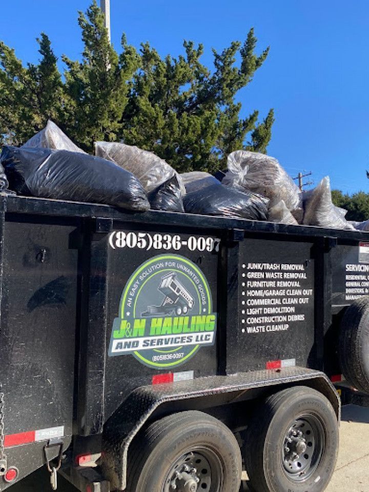A dumpster filled with bags of trash is parked on the side of the road.