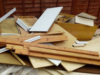 A pile of wood is sitting on the ground in front of a wooden fence.