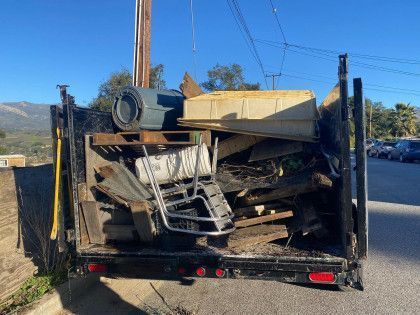 A dumpster filled with lots of junk is parked on the side of the road.