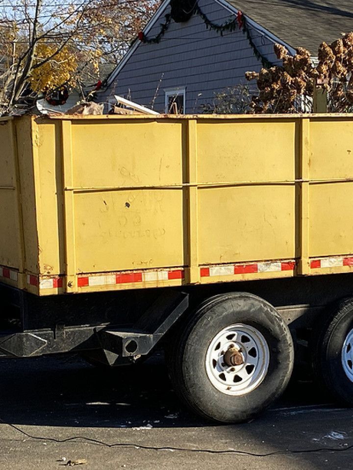 A yellow dumpster trailer is parked in front of a house.