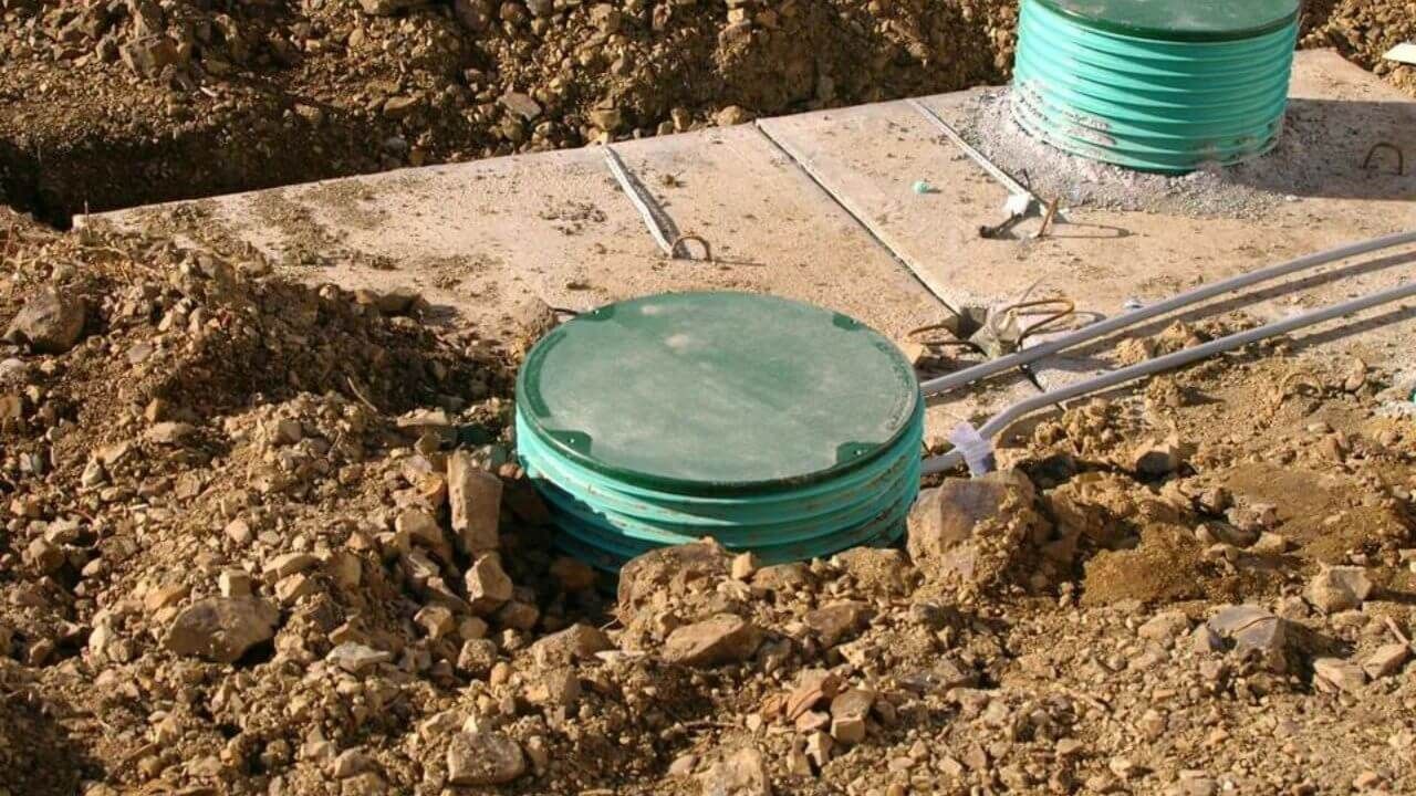 A green barrel is sitting on top of a pile of dirt.