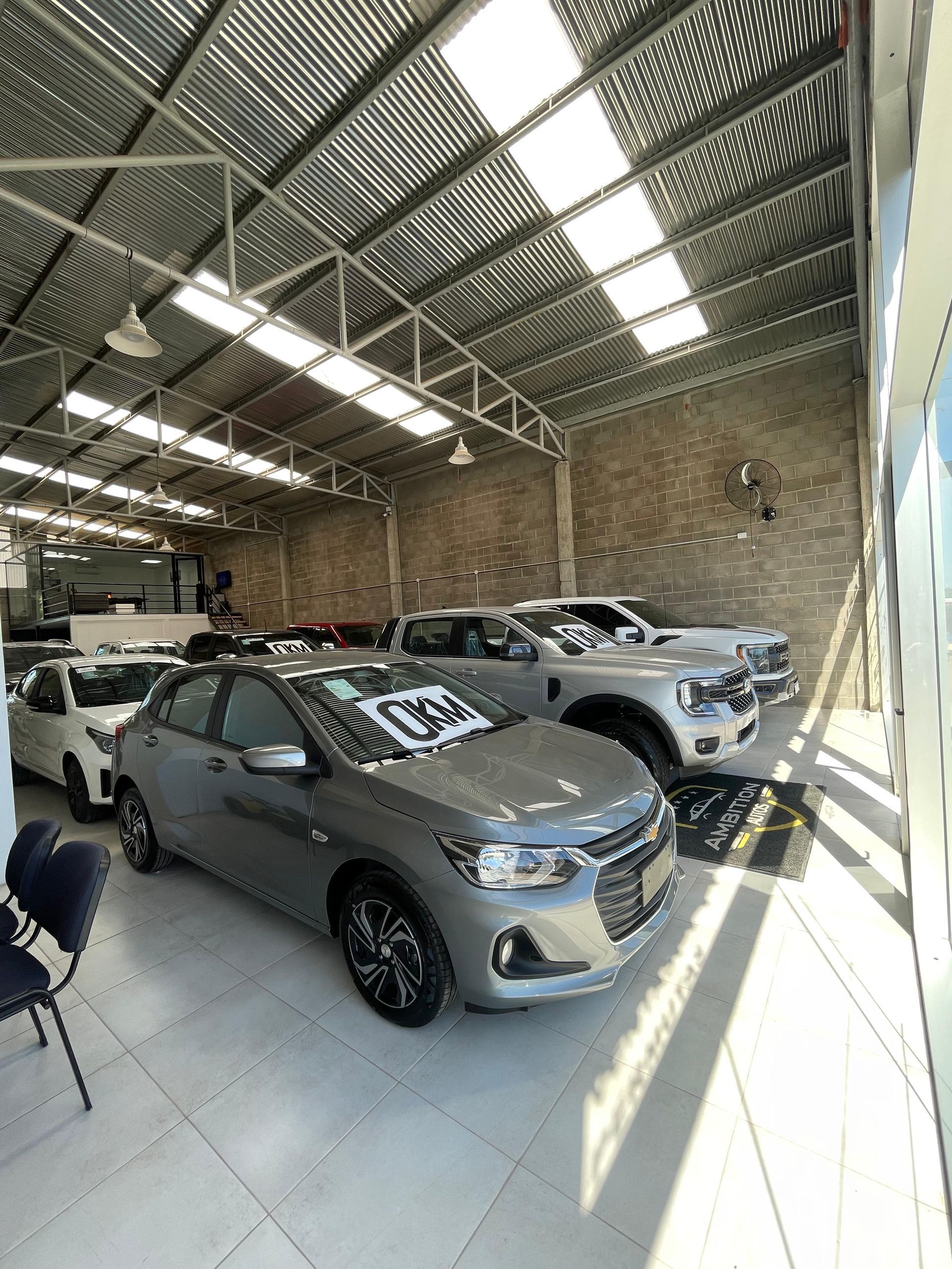 Autos estacionados dentro de un concesionario bien iluminado. Un Chevrolet gris en primer plano, una camioneta blanca y otros autos al fondo.