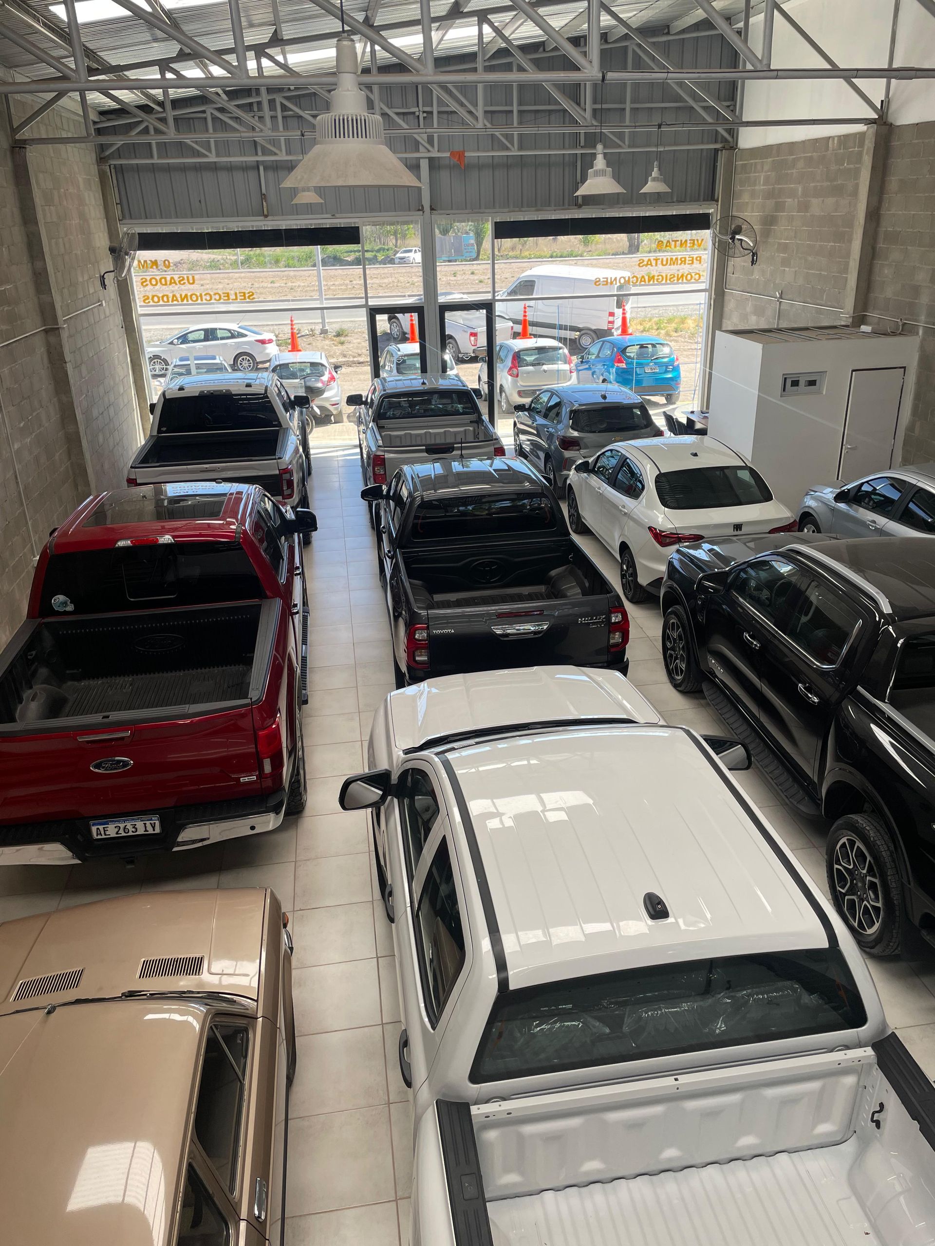 Vehículos estacionados dentro de un edificio. Se ven camionetas rojas, negras y blancas, y un sedán blanco. Interior luminoso.