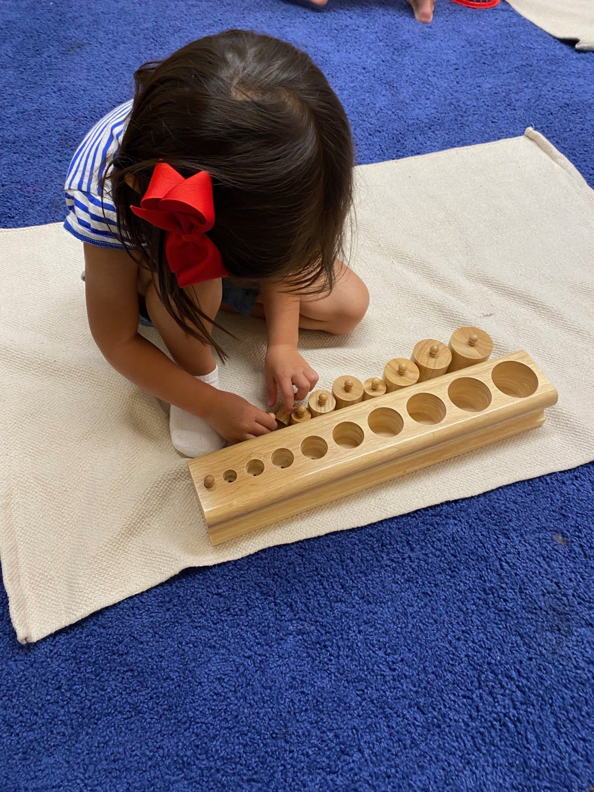 A little girl is sitting on the floor playing with a montessori wooden material.