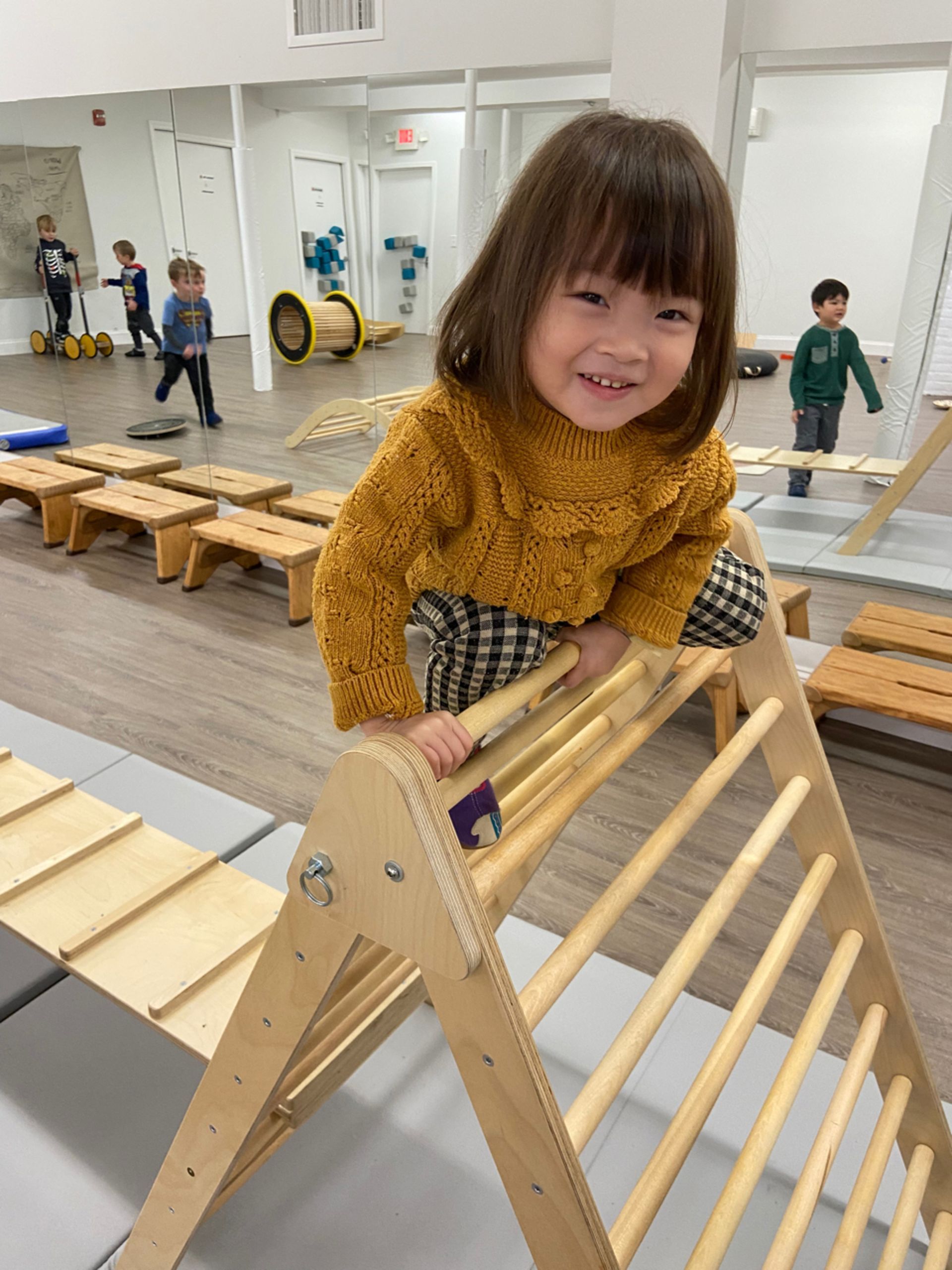 A little girl is sitting on a wooden montessori ladder in a room.