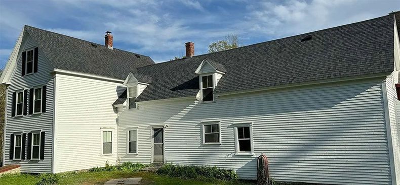 A large house with a black roof is surrounded by trees and grass.