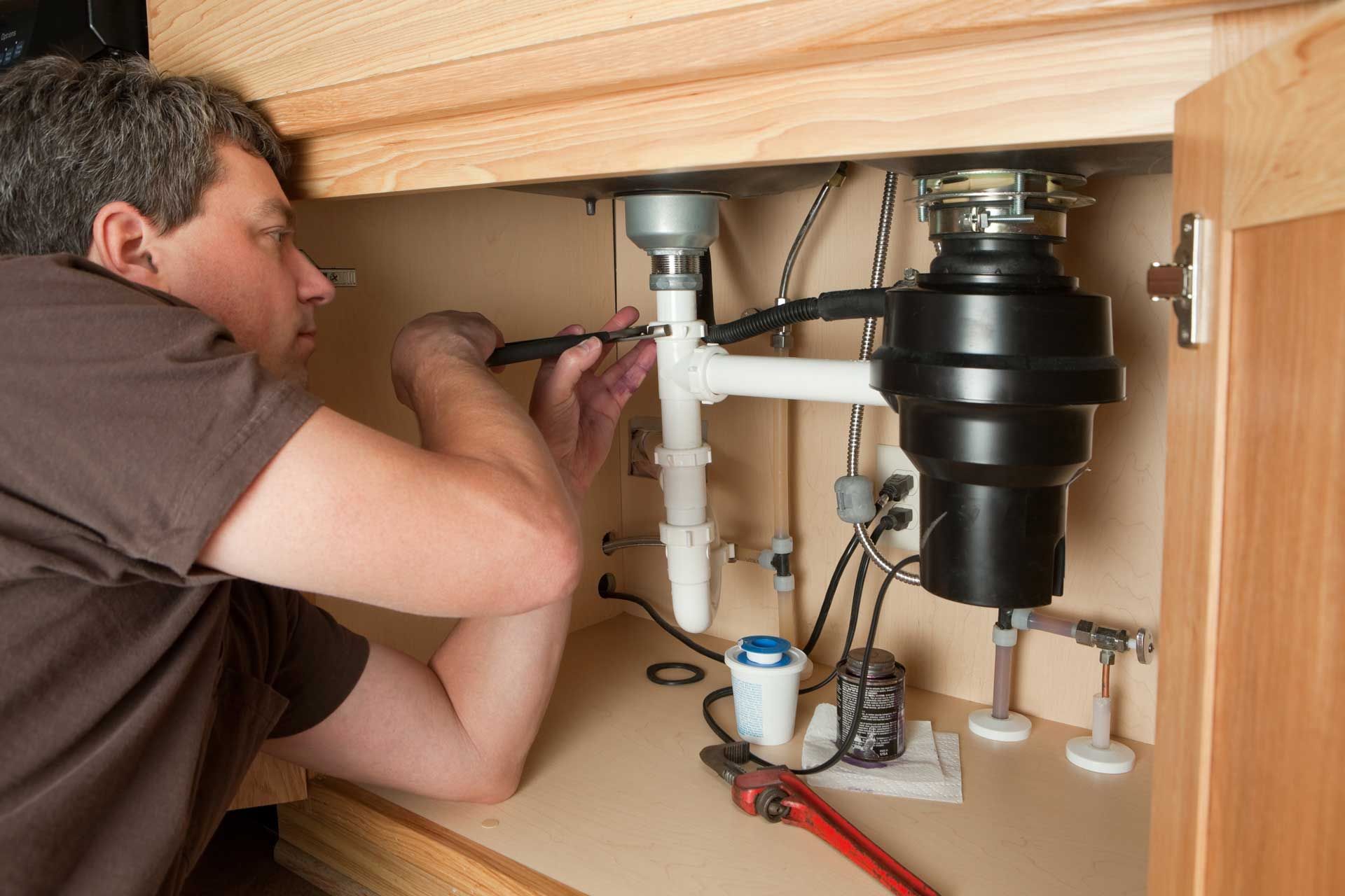 A man is fixing a garbage disposal under a sink in a kitchen.