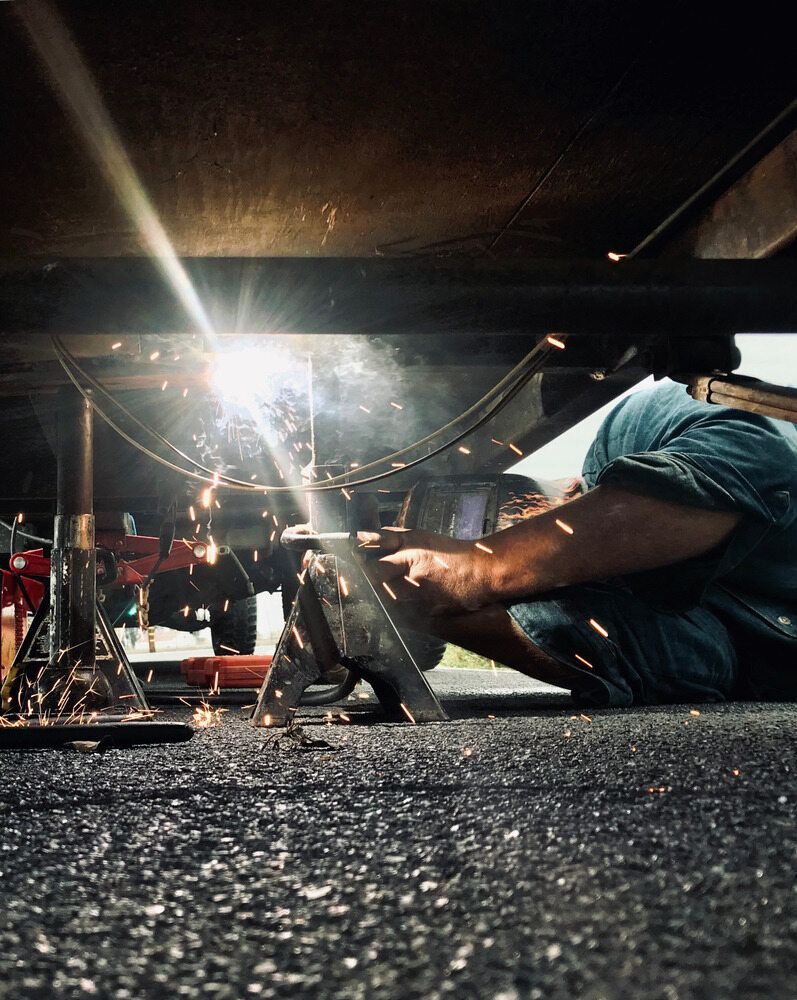 A Man Is Welding Under A Car On The Ground — KBX Mechanical In Mackay, QLD