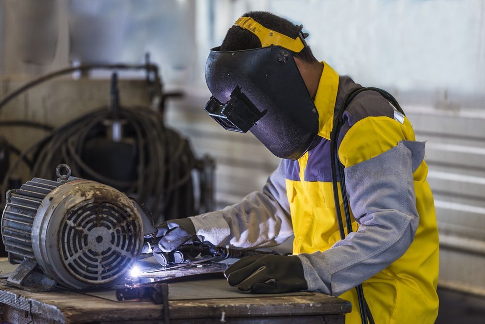 A Man Wearing A Welding Mask Is Welding A Motor — KBX Mechanical In Mackay, QLD