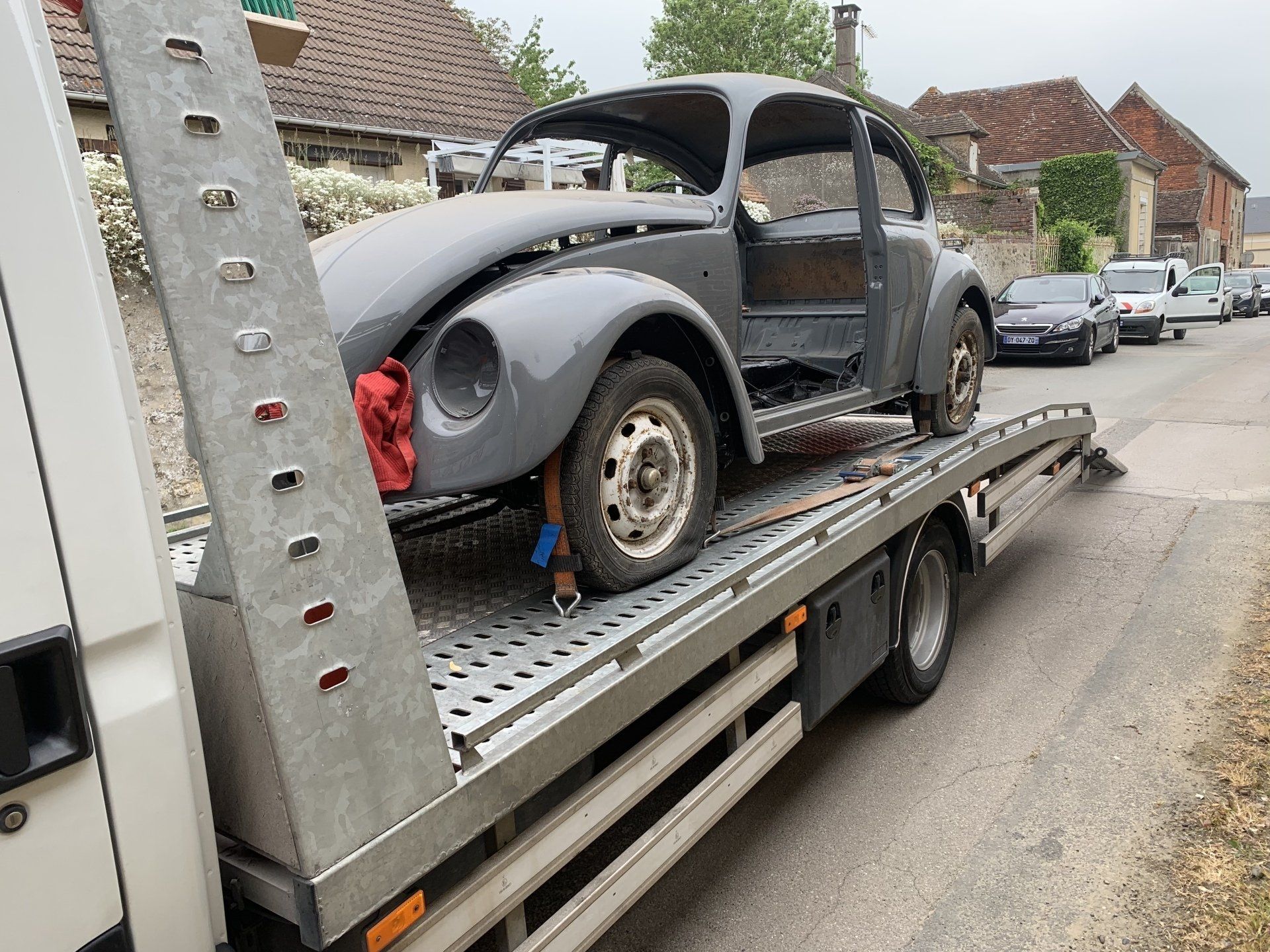 Une Coccinelle VW classique grise transportée sur une dépanneuse.