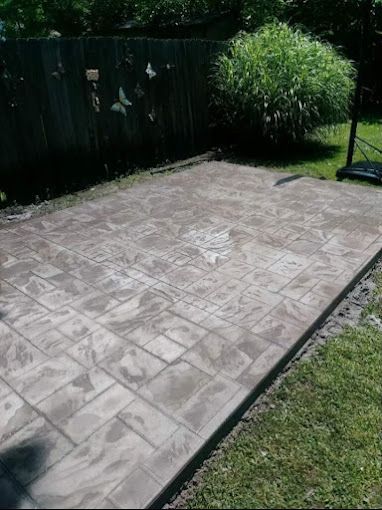 A concrete patio in a backyard with a fence in the background.