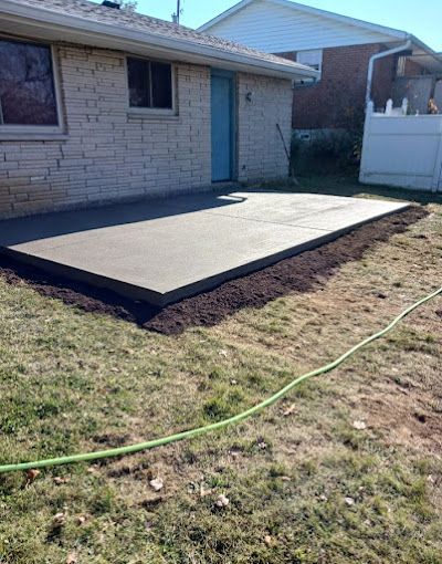 A concrete patio is being built in the backyard of a house.