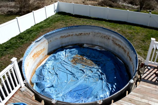 overhead view of an empty above ground pool with blue vinyl interior that is in a white fenced in yard