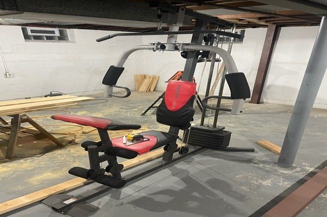 a red and black exercise machine in a basement with lumber around it