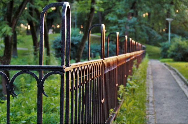 black steel fence next to a walkway surrounded by trees and bushes