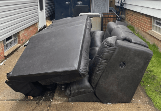 2 black couches outside next to a dumpster