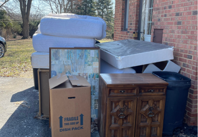 a pile of mattresses, box springs, and miscellaneous trash outside a brick house