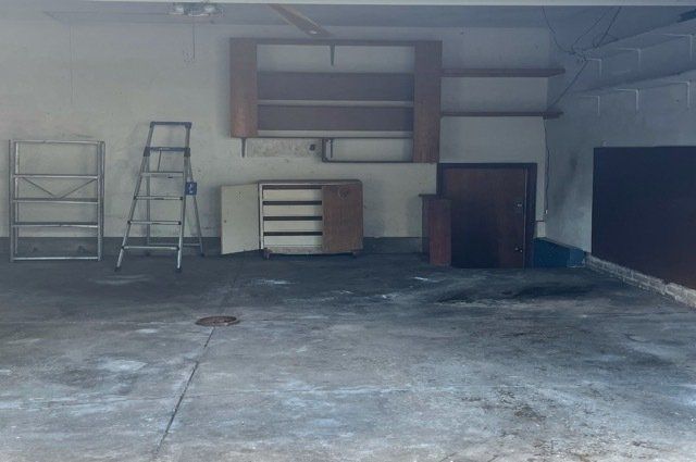 Empty garage with a ladder a door shelves and a clean concrete floor