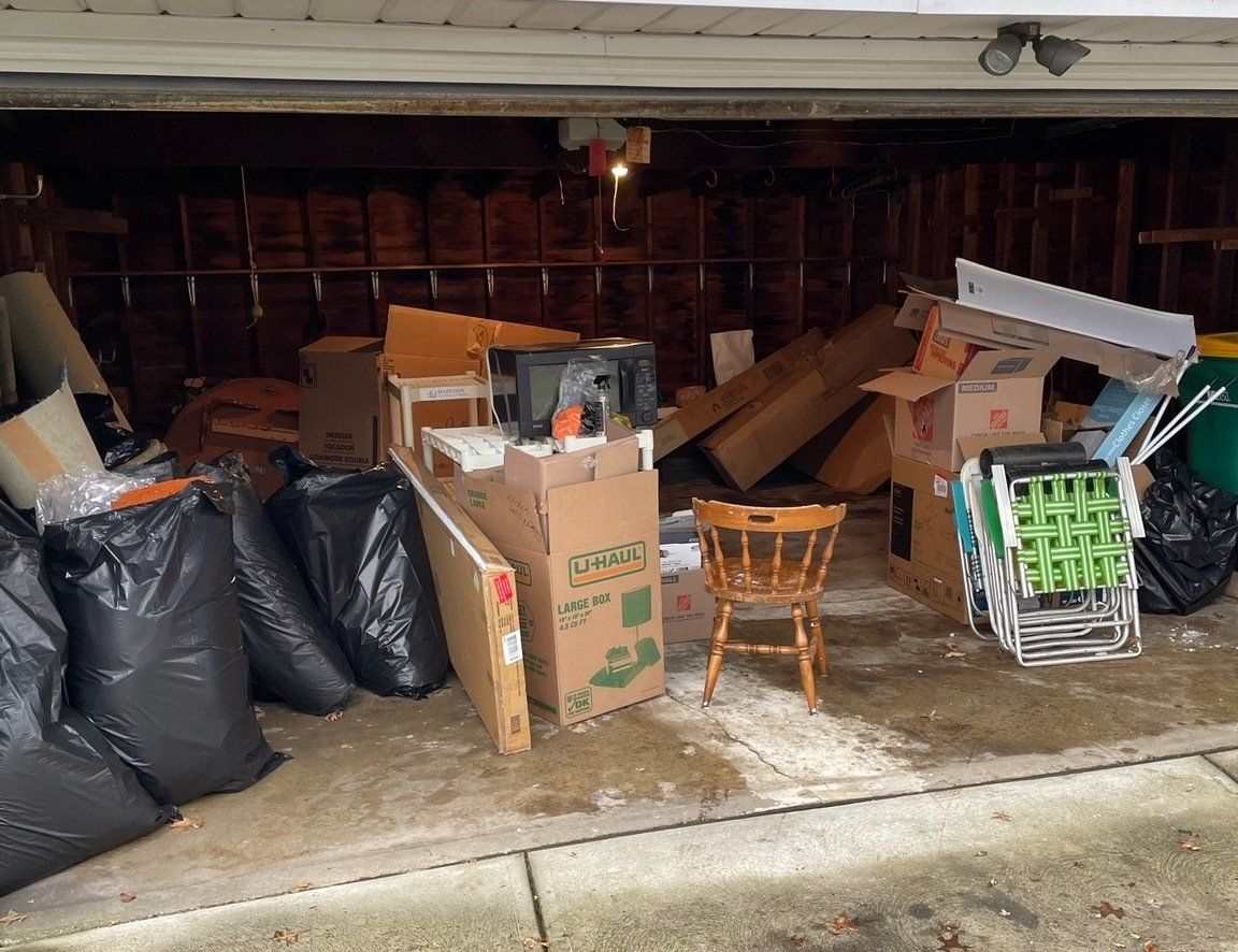 miscellaneous junk, boxes, and garbage bags inside of an open garage