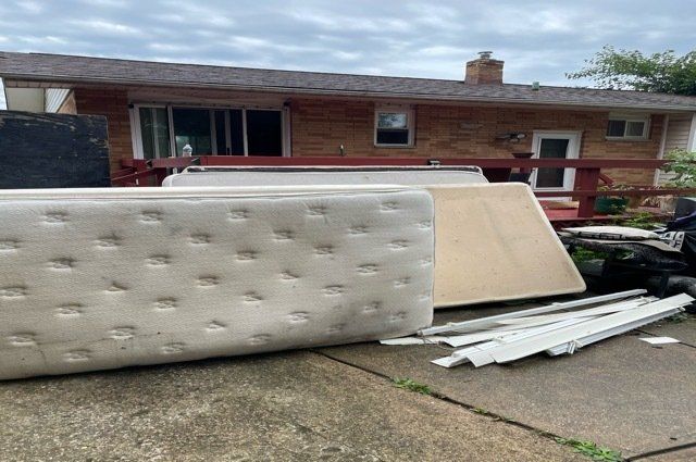 mattresses and box springs with miscellaneous junk behind a home with a red deck