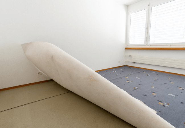 carpet that has been halfway rolled up inside of a room with white walls and a window