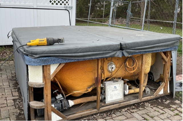 a grey hot tub that is missing side panels with a yellow tool on top of it
