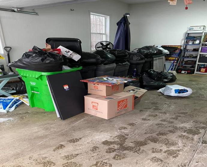 Garage that is full of several storage tubs, garbage bags, and boxes that are about to be hauled off