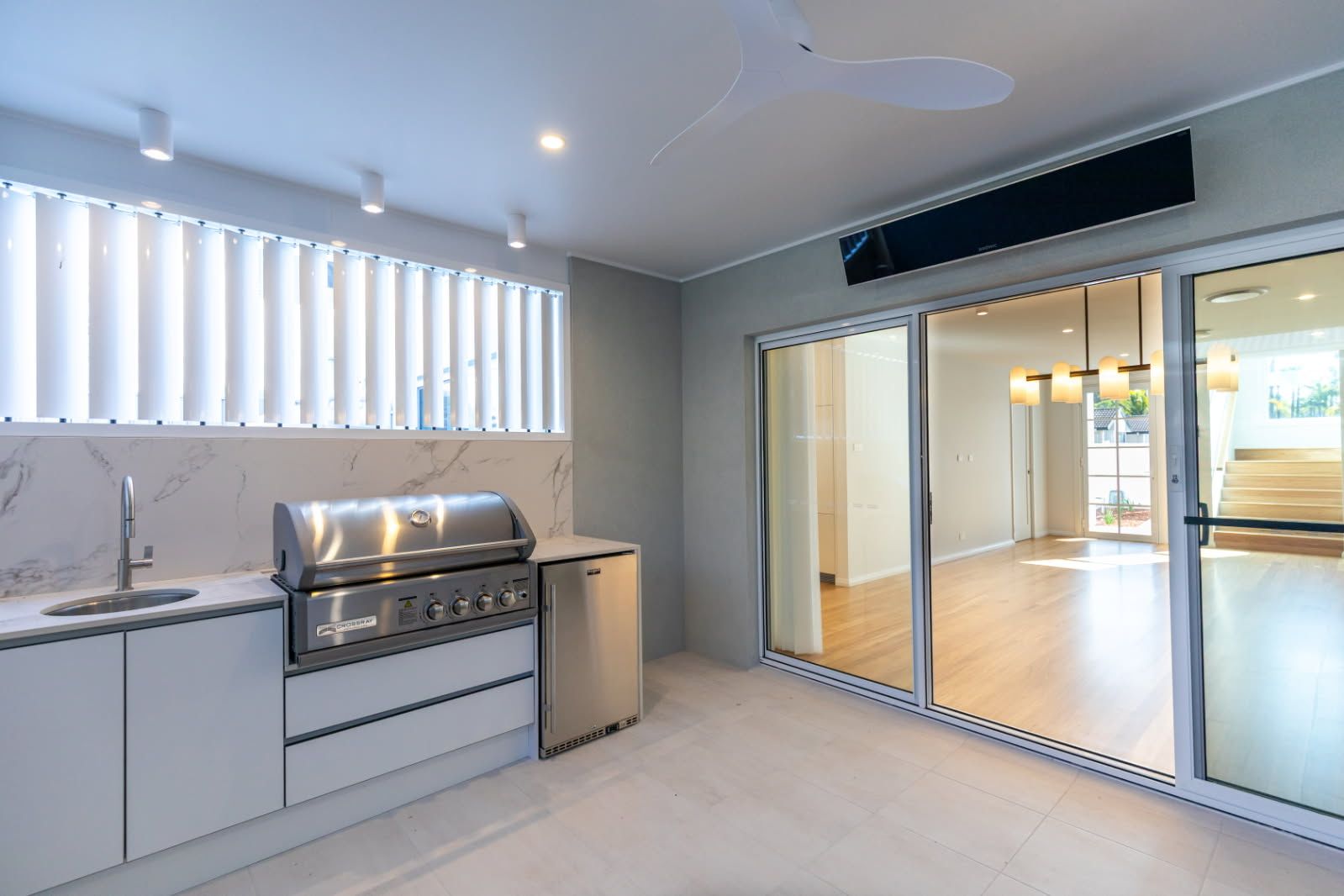 Outdoor kitchen with stainless steel grill, sink, and refrigerator, next to sliding glass doors. — Viison Kitchens & Joinery Forster In Forster, NSW