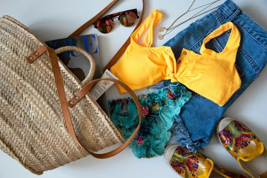 Beach bag with sunglasses, yellow bikini, denim shorts, turquoise cover-up, and floral sandals.