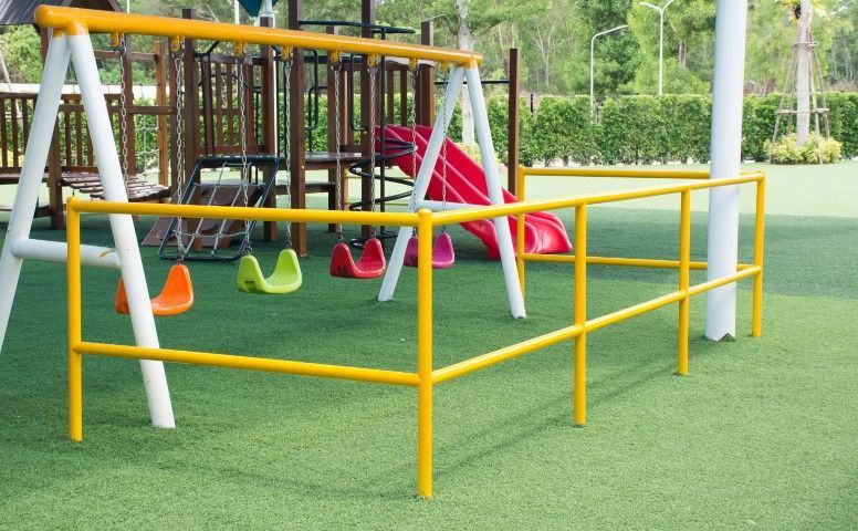 Yellow and white playground equipment: swings, slide, and railing on artificial turf.