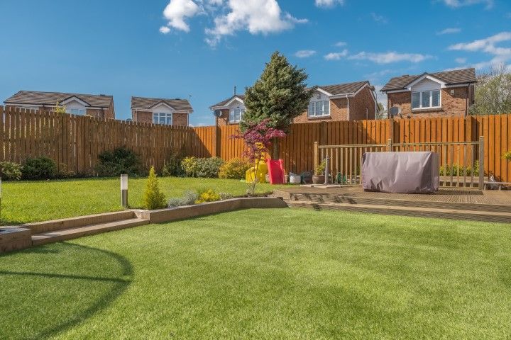 Backyard with green lawn, wooden fence, and houses under a blue sky.
