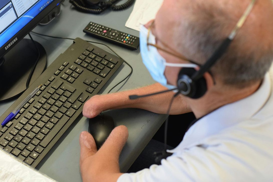 Person wearing a headset and mask using a computer mouse at a desk with keyboard and remote control